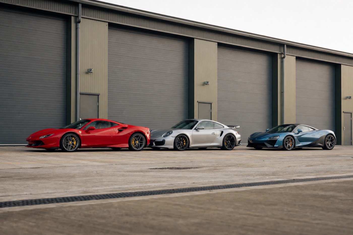 Fleet diversity in one city: a Ferrari, a Porsche and a McLaren parked in a line before a warehouse unit