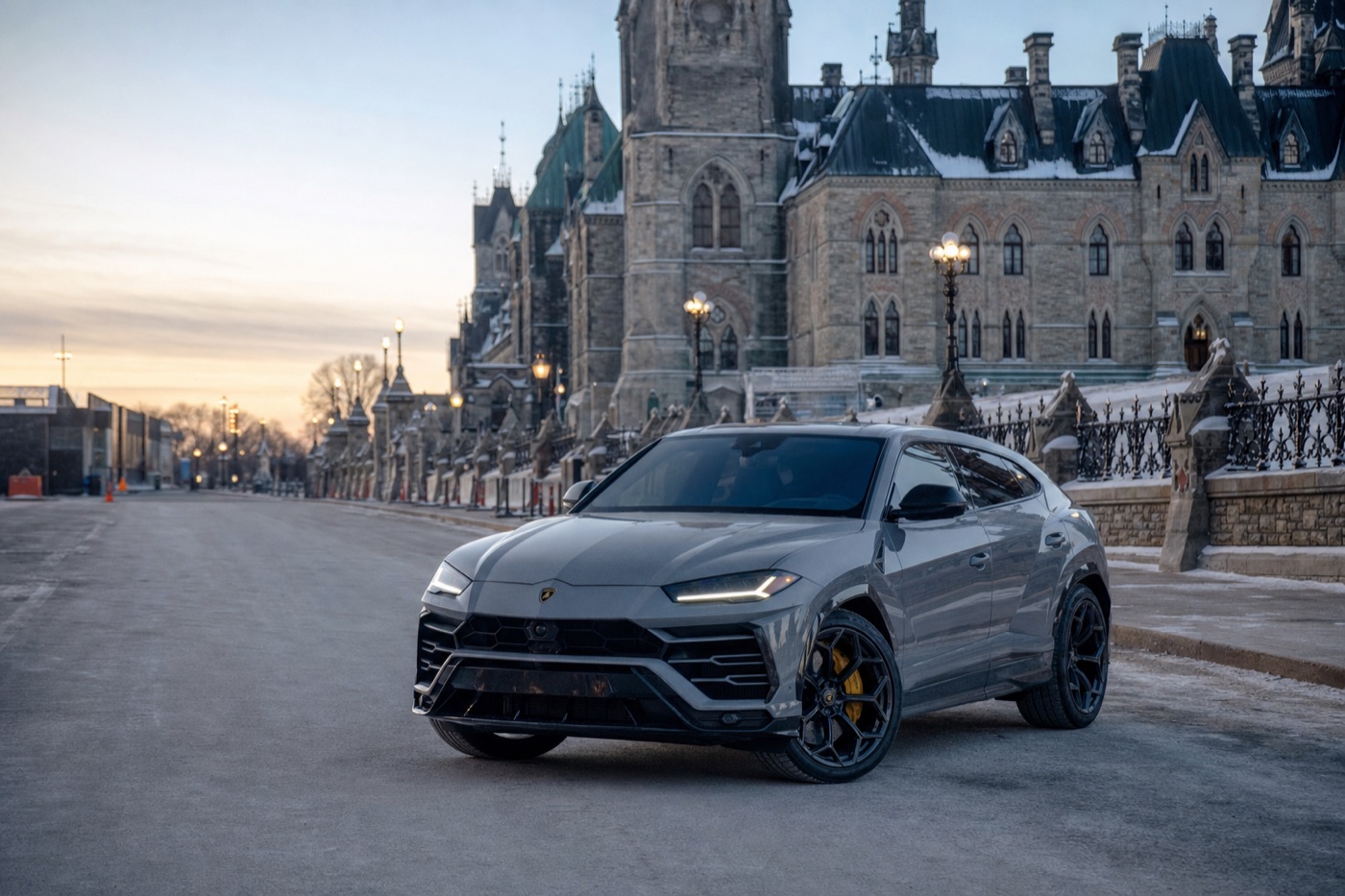 Smaller Canadian cities with few exotic rentals: a Lamborghini Urus parked before a neo-Gothic stone government building at dawn