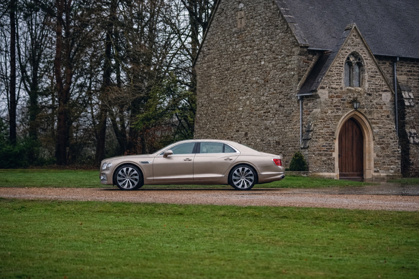 What to ask before booking a wedding car: a champagne Bentley Flying Spur parked outside a stone church entrance
