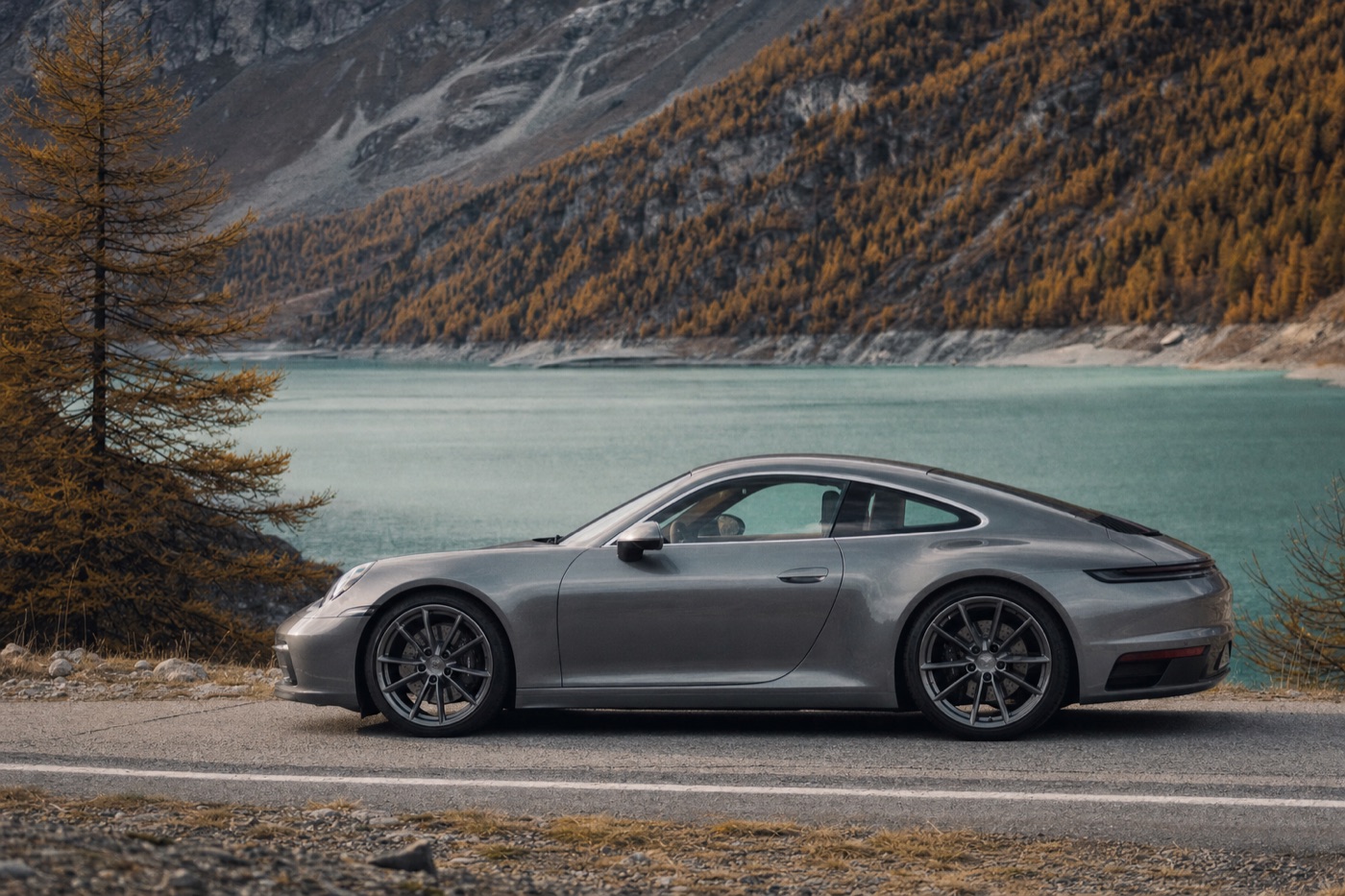 Renting a luxury car in Canada: a Porsche 911 on a mountain road beside a turquoise lake with golden larches