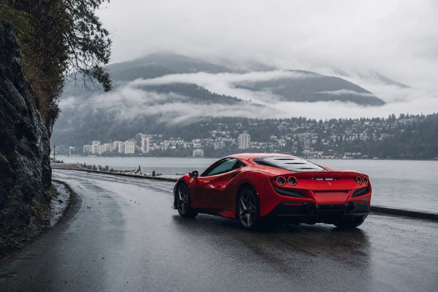 How much a luxury car rental costs in Canada: a Ferrari on a waterfront road in Vancouver with mountains behind in rain