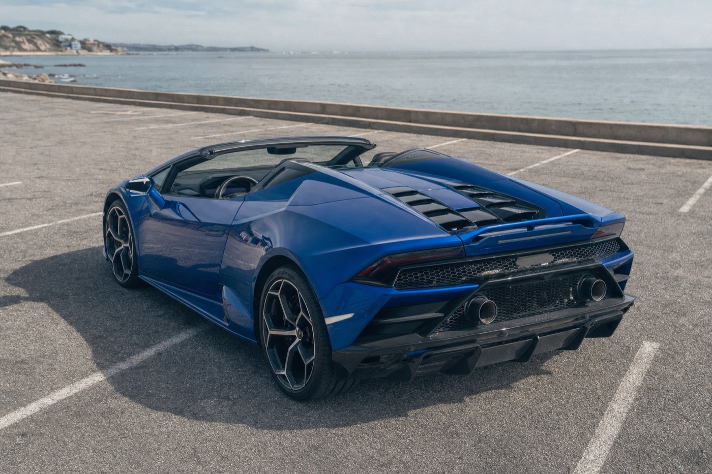 Which Huracán specification to reserve: a blue Huracán EVO Spyder with its roof retracted parked beside the ocean