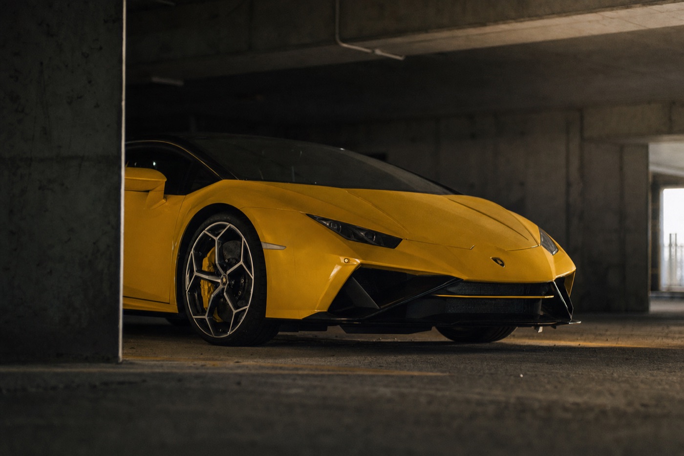 Lamborghini Huracán vs Urus rental: a Huracán in a concrete parking garage lit by directional spotlights